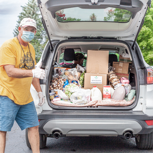 Men volunteering at Families Matter Food Pantry by filling up a person's trunk with fresh food