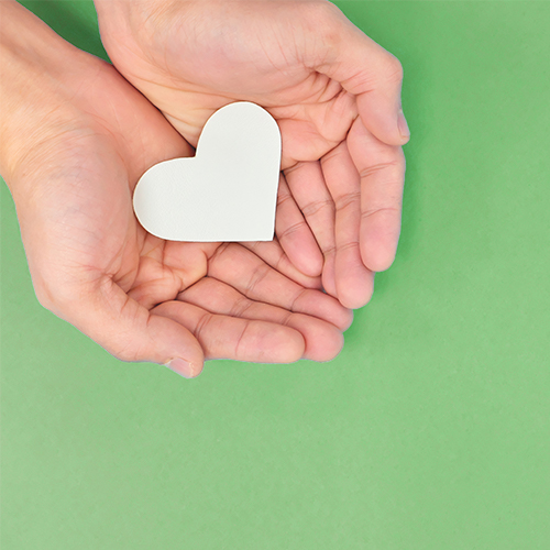 Man holding a white paper heart in his open cupped hands on top of a green table top