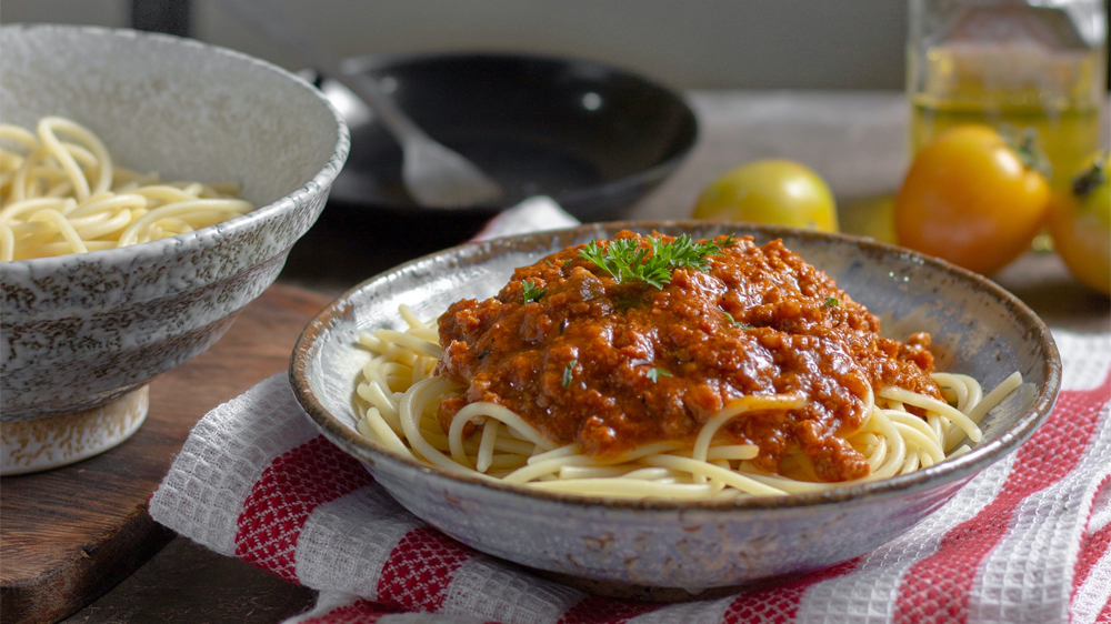 Linguine pasta with red meat sauce and parsley in a ceramic bowl on top of a wood table